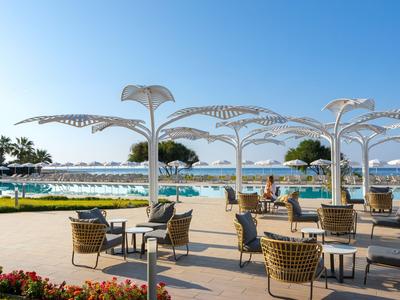 Terrasse avec tables et chaises près d'une piscine avec vue sur des palmiers et un ciel bleu.