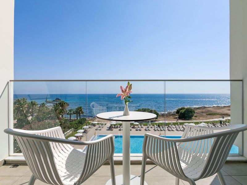 Balkon mit zwei weißen Stühlen, Tisch und Meerblick unter blauem Himmel.