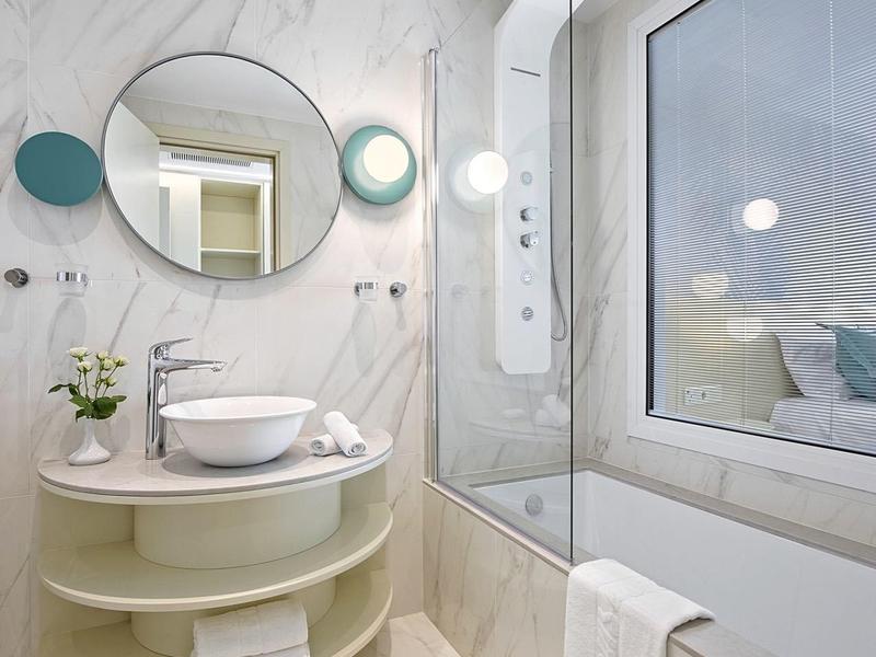 Helles Badezimmer mit rundem Spiegel, Waschbecken auf Ablage und Badewanne neben großem Fenster.