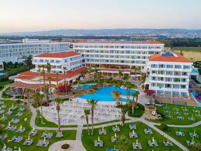 Großes Hotelresort mit mehreren Gebäuden, Pool und umliegenden Liegestühlen auf grünem Rasen.