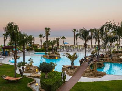 Poolbereich mit Palmen und Blick auf das Meer bei Sonnenuntergang in einem Resort.