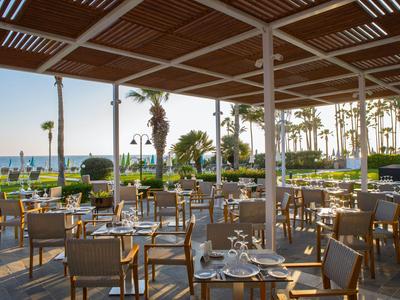 Offene Terrasse eines Hotels mit gedeckten Tischen und Blick auf Palmen und Meer.
