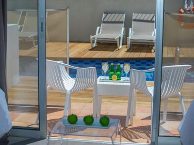Balkon mit zwei weißen Stühlen, Tisch mit Getränken und Blick auf zwei Liegestühle.