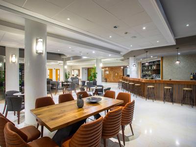 Moderner Hotel-Lounge-Bereich mit Holztischen, Ledersesseln und großer Bar.