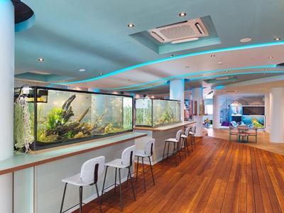 Moderner Hotelraum mit großem Aquarium, weißen Stühlen und Holzboden.