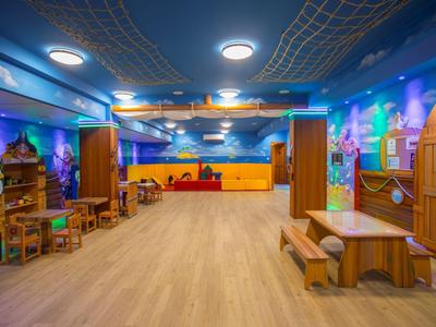 Buntes Hotel-Spielzimmer mit Holzmöbeln und bemalten Wänden unter Deckenleuchten.