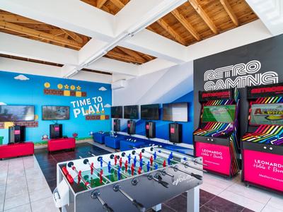 Ein bunter Spielraum mit Tischfußball, Retro-Arcade-Spielen und Fernsehern unter einem Holzbalkendach.