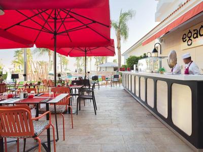 Außenbereich einer Hotelbar mit roten Sonnenschirmen und Sitzgelegenheiten.