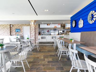 Moderner Frühstücksraum mit weißen Stühlen, Holztischen und blauer Wand mit großen Uhren.