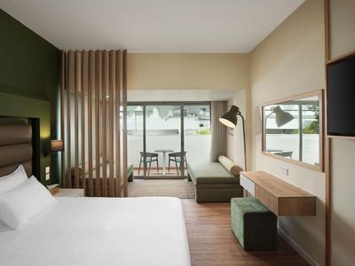 Modern eingerichtetes Hotelzimmer mit Bett, Sitzbereich und Balkon mit Blick auf das Wasser.