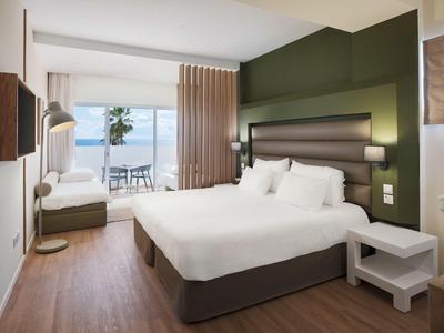 Modernes Hotelzimmer mit Doppelbett, Holzboden und Blick auf die Terrasse und das Meer.
