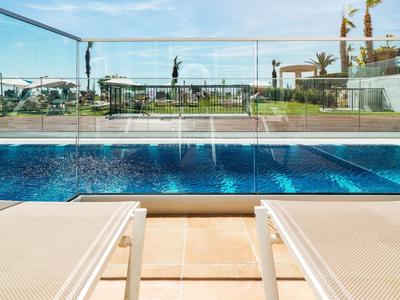 Ein klarer blauer Pool mit zwei Liegestühlen auf der Terrasse und Blick auf Gärten und Himmel.