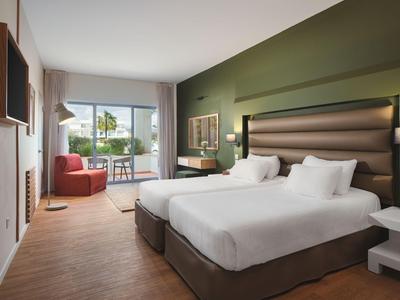 Modernes Hotelzimmer mit zwei Betten, grünem Akzentwand und Balkon mit Aussicht.