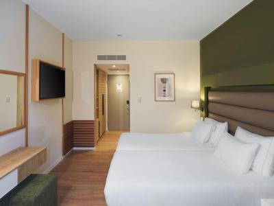 Modern eingerichtetes Hotelzimmer mit zwei Betten, Flachbildfernseher und Holzfußboden.