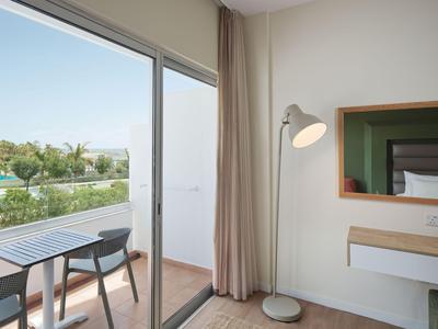 Moderner Hotelzimmerbereich mit Zugang zu Balkon und Blick auf Pool und Palmen.