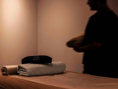 Ein Handtuch und ein Kissen auf einer Massageliege in einem ruhigen Raum mit gedämpftem Licht.