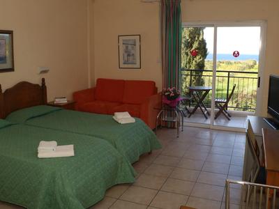 Hotelzimmer mit zwei Betten, grünem Bettüberwurf, rotem Sofa, Fernseher und Balkon mit Aussicht.