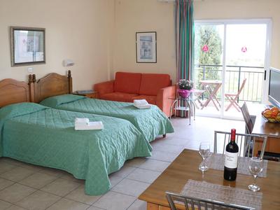 Chambre d'hôtel avec deux lits simples, couvertures vertes, canapé et balcon avec table et chaises.