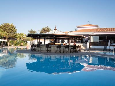 Grande piscina esterna con bar e aree salotto accanto agli edifici dell'hotel sotto un cielo sereno.