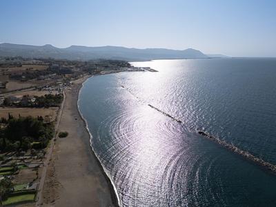 Linea costiera con spiaggia sabbiosa, onde e montagne sullo sfondo sotto il sole.