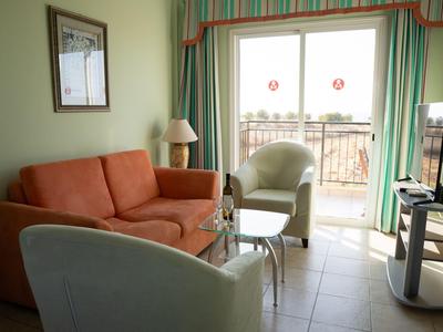 Soggiorno con divano, poltrone, tavolo, TV e accesso a balcone con vista.