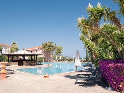 Piscina dell'hotel con lettini e vegetazione rigogliosa sotto un cielo azzurro limpido.