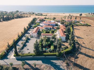 Vista aerea di un hotel isolato con tetti rossi e giardino, circondato da campi vicino al mare.
