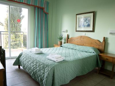 Camera d'albergo luminosa con letto matrimoniale, copriletto verde e balcone con vista esterna.