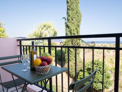 Balcone con tavolo verde, due sedie, cesta di frutta e due bottiglie d'acqua di vetro.