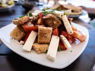 Insalata fresca con pomodori, crostini di pane e formaggio su un piatto bianco.