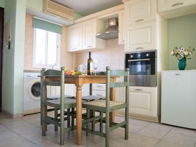 Piccola cucina con pareti verde chiaro, tavolo di legno, quattro sedie e elettrodomestici moderni.