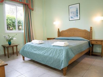 Camera d'hotel luminosa con letto grande, copriletto verde e finestra con tende.