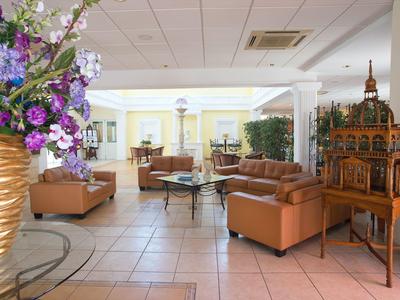 Heller Wartebereich mit braunen Ledersofas, Glastisch, großem Blumenarrangement und kunstvollem Modell.