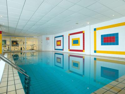 Piscine intérieure avec œuvres murales géométriques colorées et main courante en acier inoxydable.