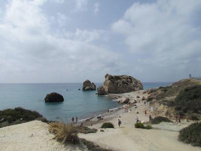 Kleiner Sandstrand mit Felsen im Wasser, umgeben von karger Vegetation und bewölktem Himmel.