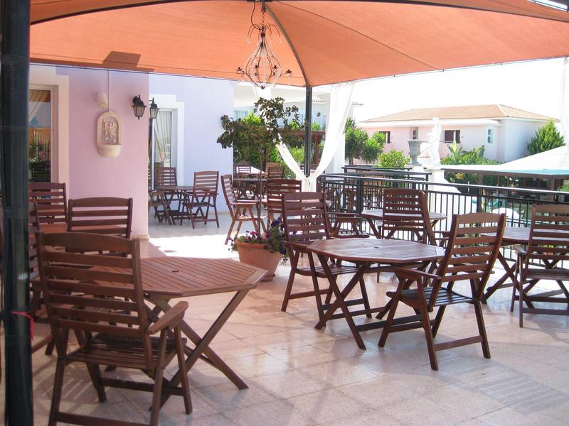 Überdachte Terrasse mit braunen Holzstühlen und Tischen, heller Bodenbelag und Sonnenlicht.