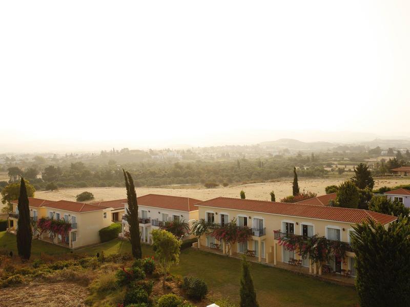 Mehrere einstöckige Häuser mit roten Dächern und Bäumen in hügeliger Landschaft bei Nebel.