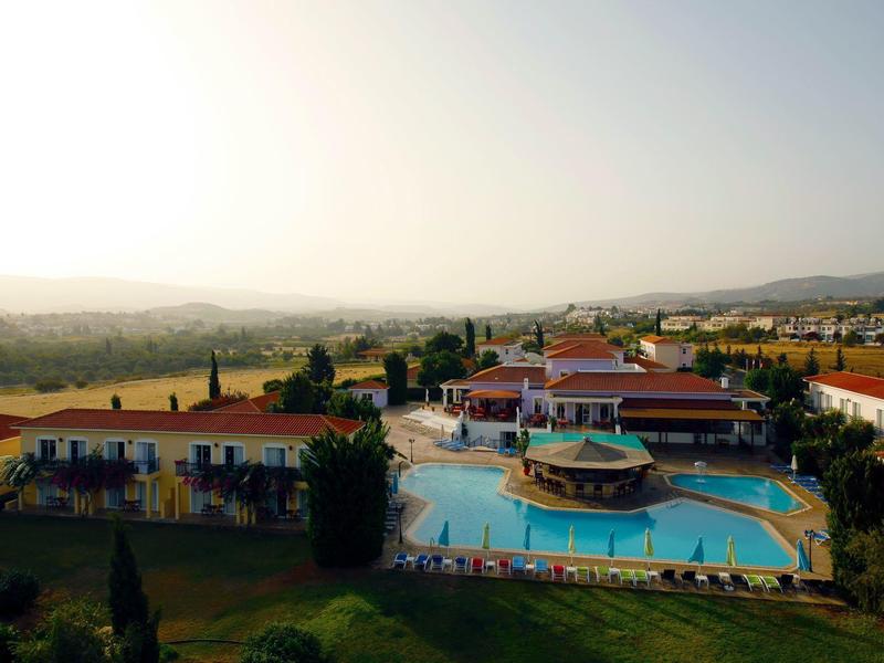 Große Außenpoolanlage mit rundem Poolhaus, umgeben von Gebäuden und Hügeln im Hintergrund bei Abendlicht.
