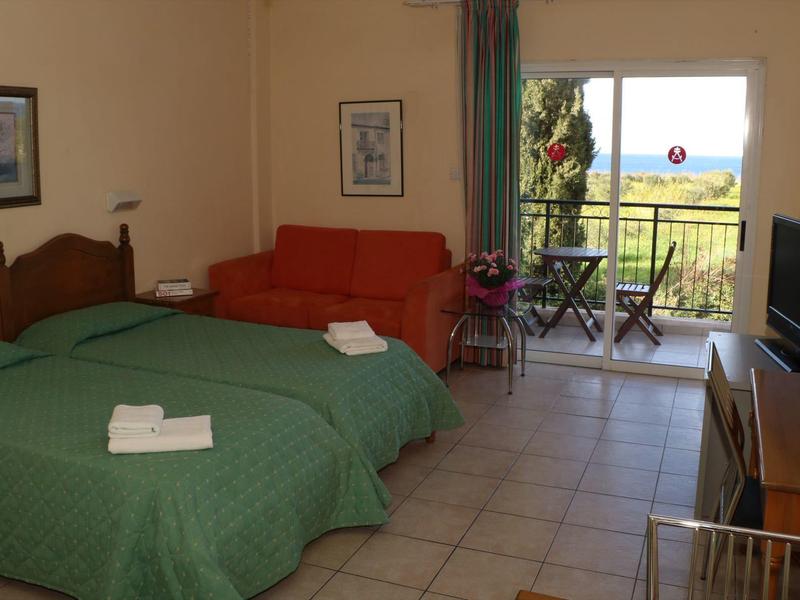 Hotelzimmer mit zwei Betten, grünem Bettüberwurf, rotem Sofa, Fernseher und Balkon mit Aussicht.