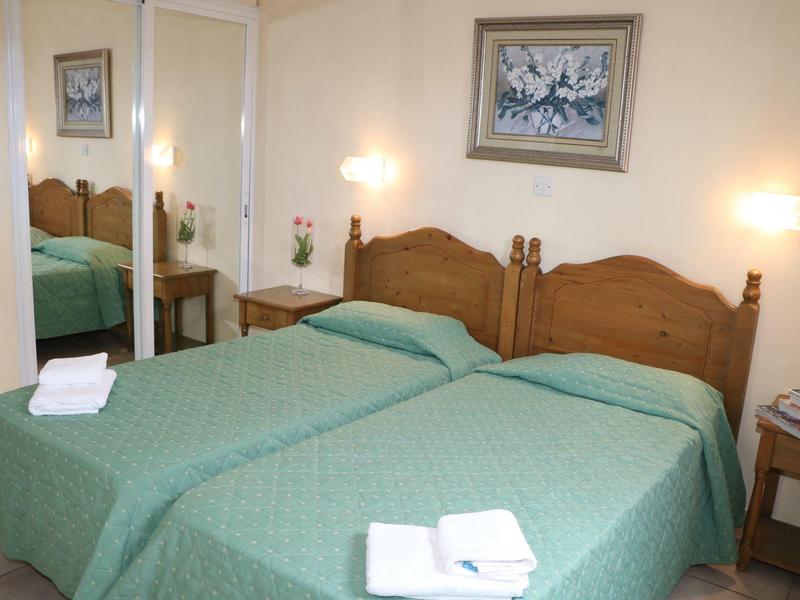 Zwei Einzelbetten mit grünen Decken, je ein Handtuch, Holzmöbel und Spiegel an der Wand.