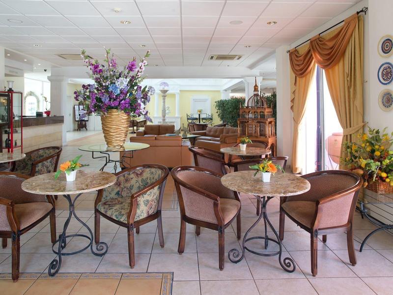 Ein heller Gastraum mit runden Tischen, braunen Stühlen und großen Blumenarrangements.