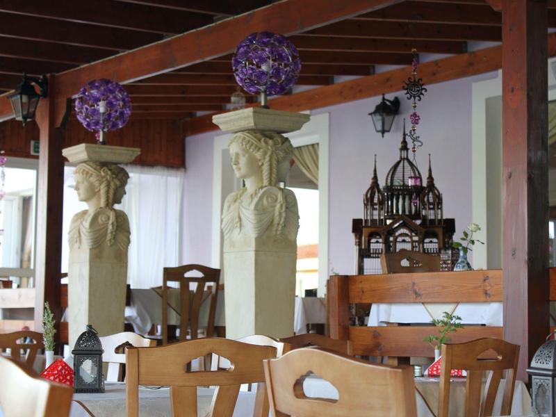 Offener Gastraum mit Holzstühlen, kunstvollen Säulen und violetten Deko-Lampen an der Decke.