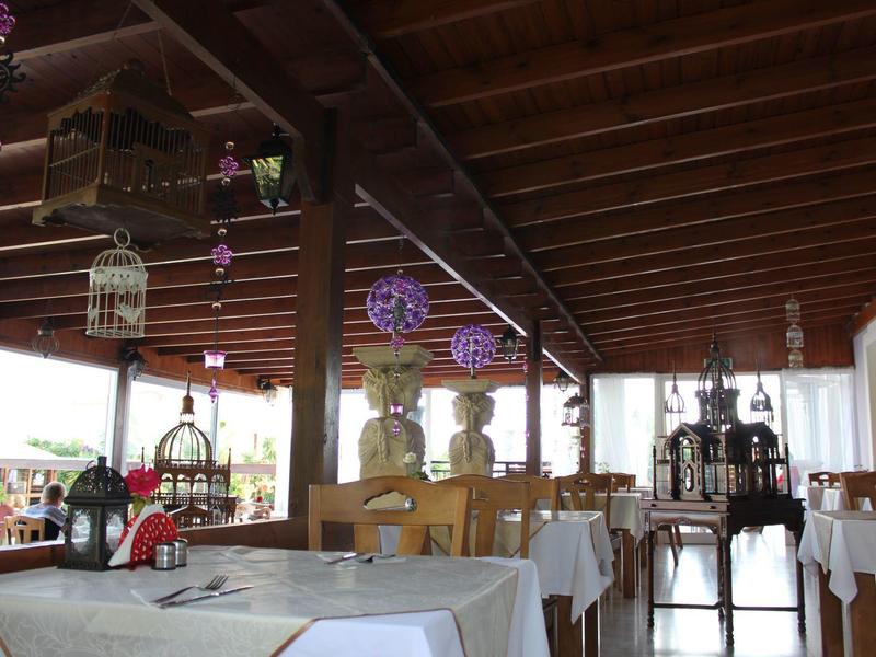 Überdachte Terrasse mit Holzdecke, mehreren Tischen, Blumen und dekorativen Hängelampen.