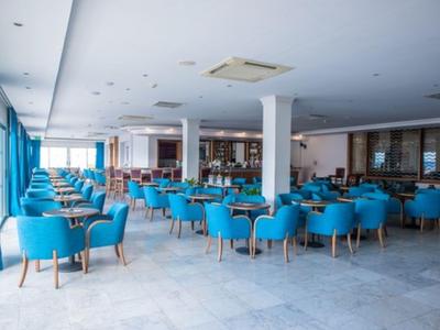 Grote eetzaal met blauwe stoelen, houten tafels en grote ramen.