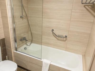 Helles Badezimmer mit Badewanne, geteilter Glasdusche, Handtuch und WC in neutralen Farben.