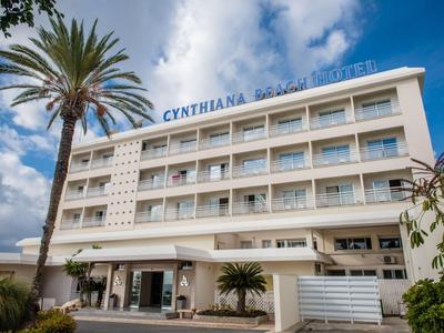 Vier verdiepingen tellend hotelgebouw met een grote palmboom ervoor onder een blauwe lucht.