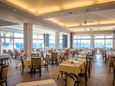 Licht, modern restaurant met veel tafels en stoelen, grote ramen met uitzicht op zee.