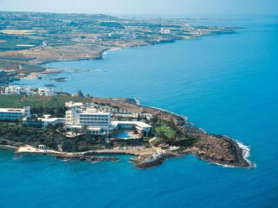 Küstenlinie mit Hotels, Felsen und blauem Meer unter klarem Himmel, Umgebung zeigt Siedlungen.