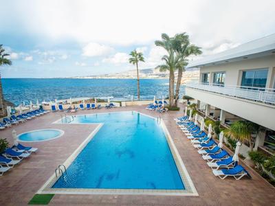 Großer Pool mit blauen Liegestühlen, Palmen und Blick aufs Meer an einem sonnigen Tag.