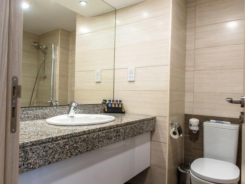 Helles Badezimmer mit grauer Granit-Arbeitsplatte, rundem Waschbecken, Spiegel und Toilettenanlage.